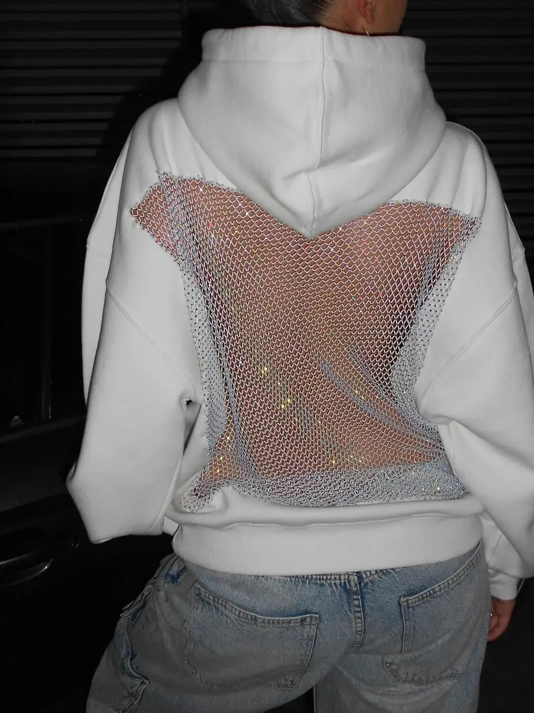 Person wearing a white hoodie with a decorative mesh panel on the back.